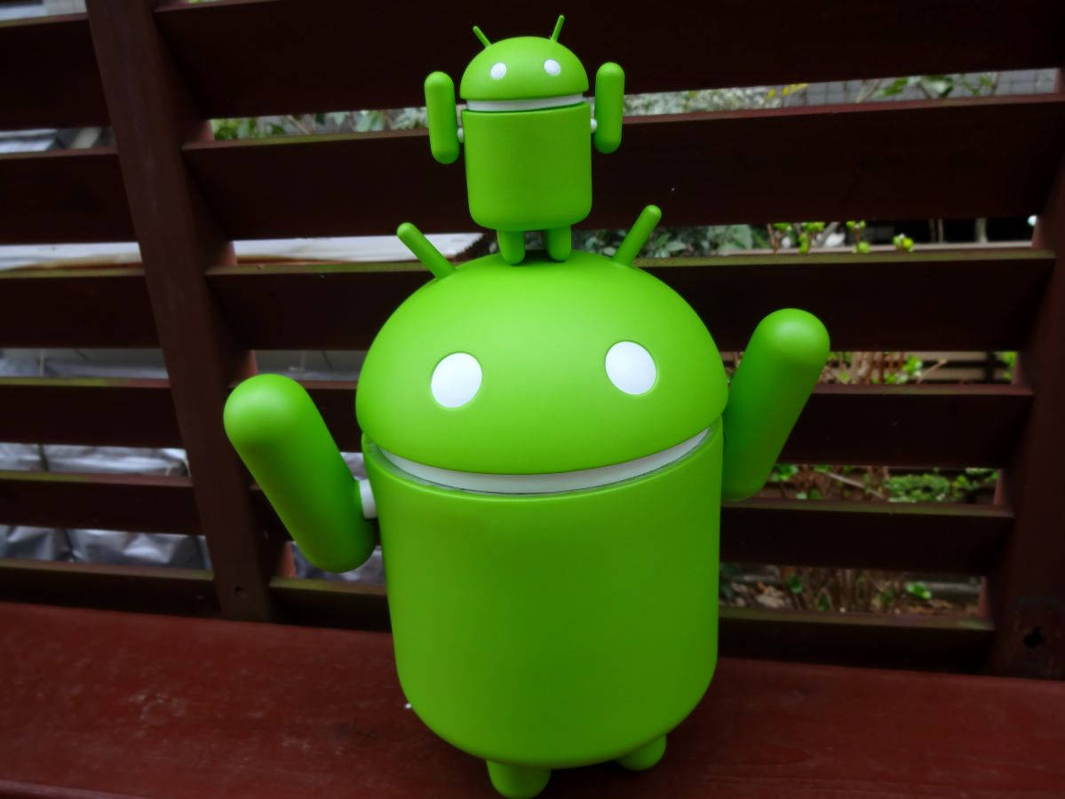 En grøn Android-legetøj står på en træbænk Wallpaper