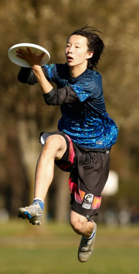Fondode Pantalla De Un Atleta Asiático Saltando Mientras Juega Ultimate Frisbee Con Un Androide.