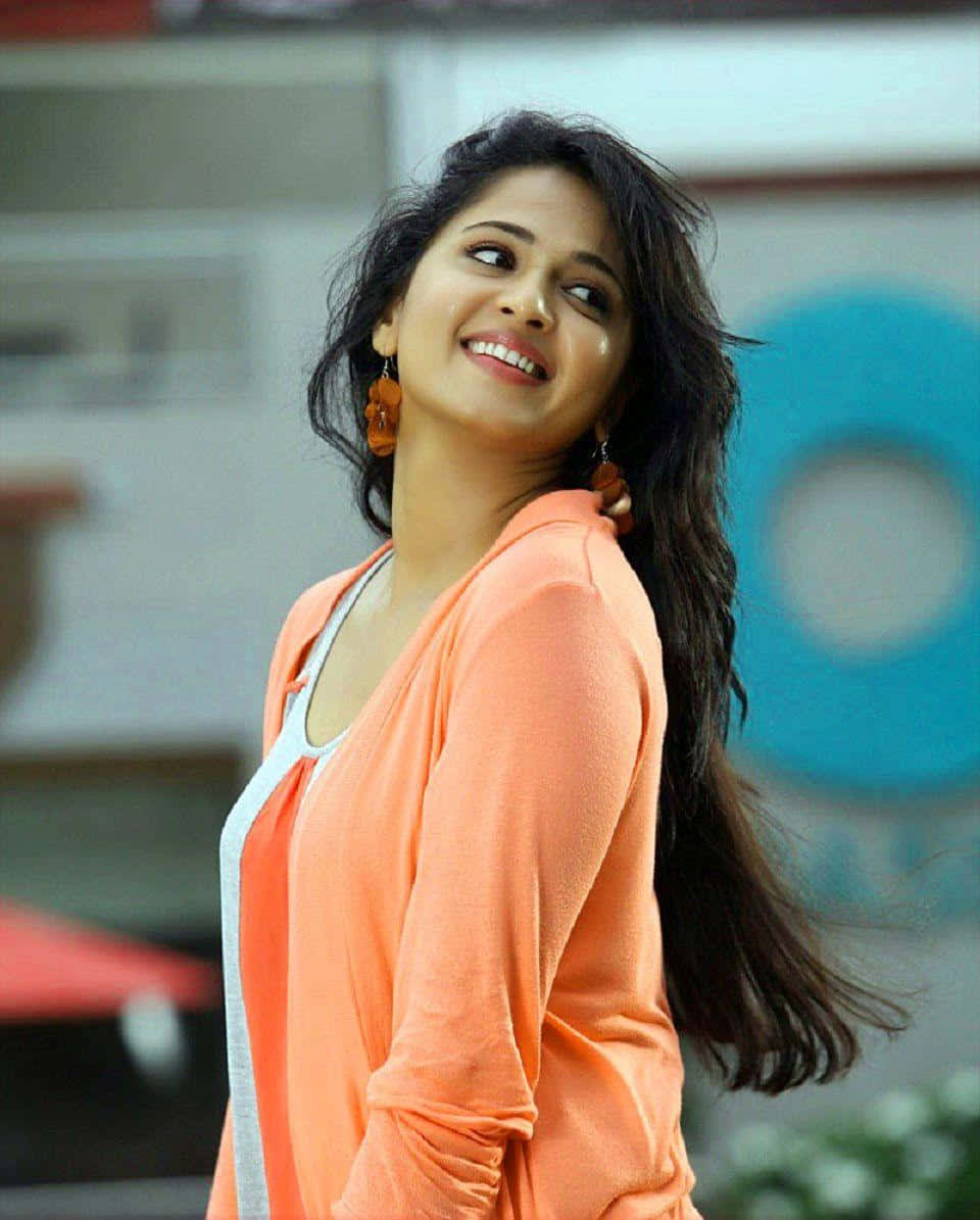 Anushka Shetty Glimlachend In Oranje Top Achtergrond