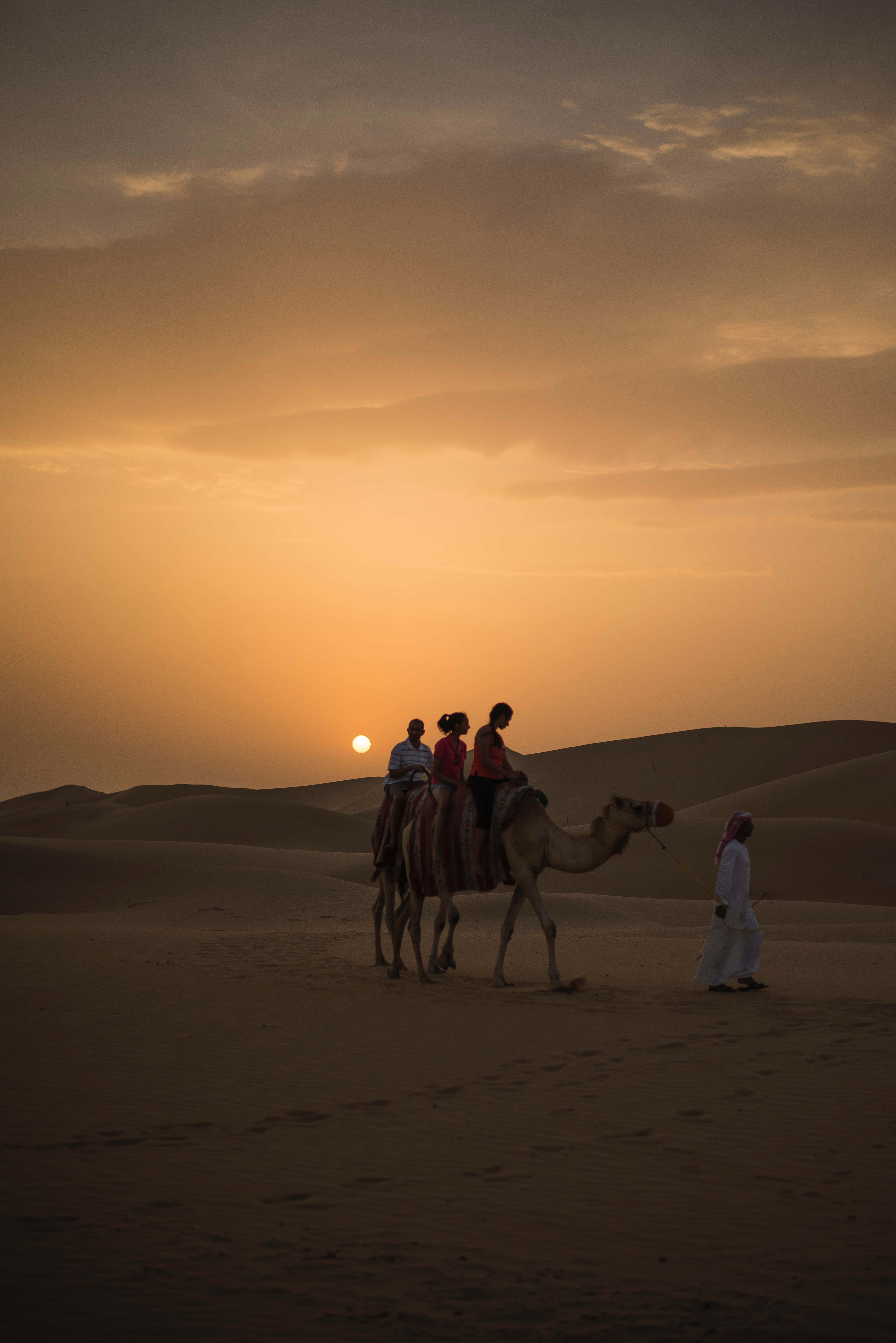 Meaningful Arabic Calligraphy Wallpaper — Silhouetted travelers ride a camel across golden desert dunes as the sun sets behind distant sand hills.