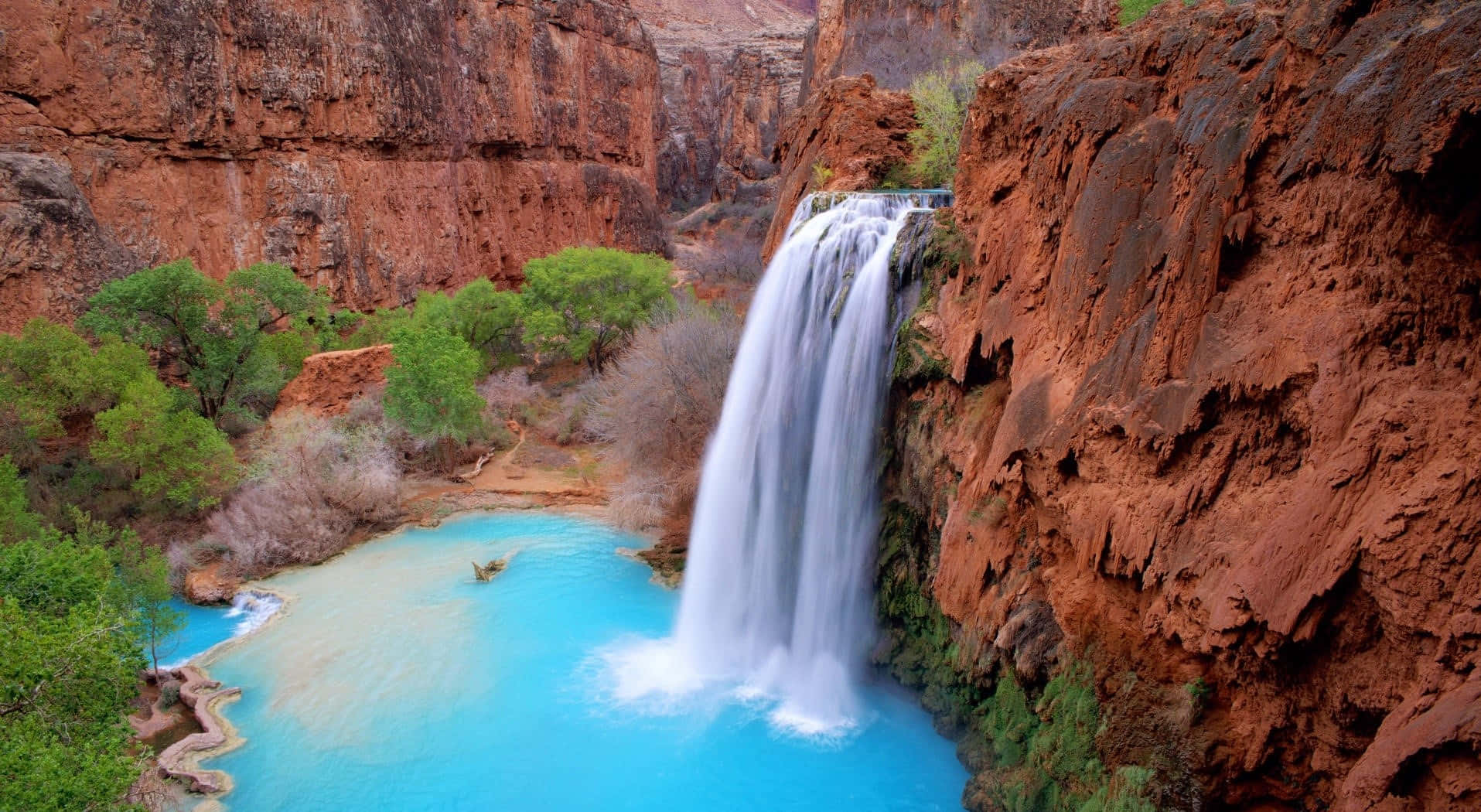 A Waterfall In A Canyon With Blue Water