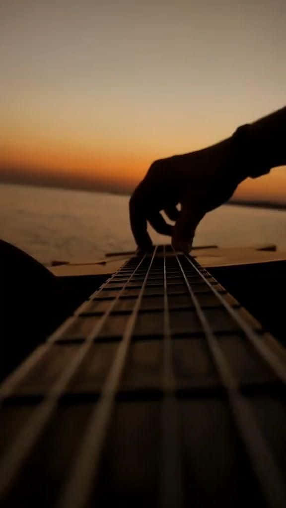 En person spiller akustisk guitar ved solnedgang Wallpaper