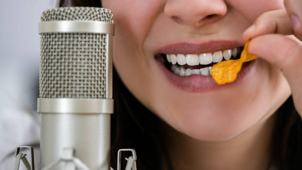 Einefrau Isst Ein Stück Käse Und Spricht Dabei In Ein Mikrofon. Wallpaper