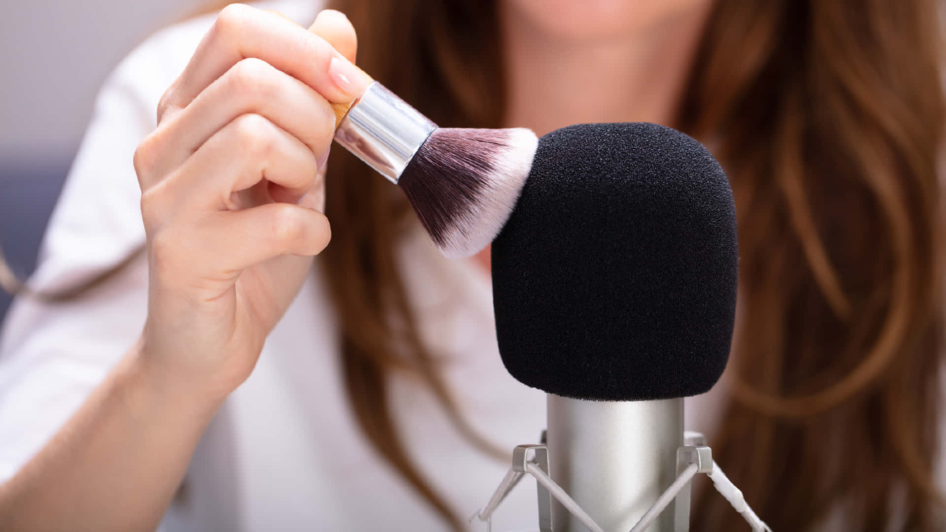Einefrau Benutzt Vor Einem Mikrofon Einen Make-up-pinsel. Wallpaper