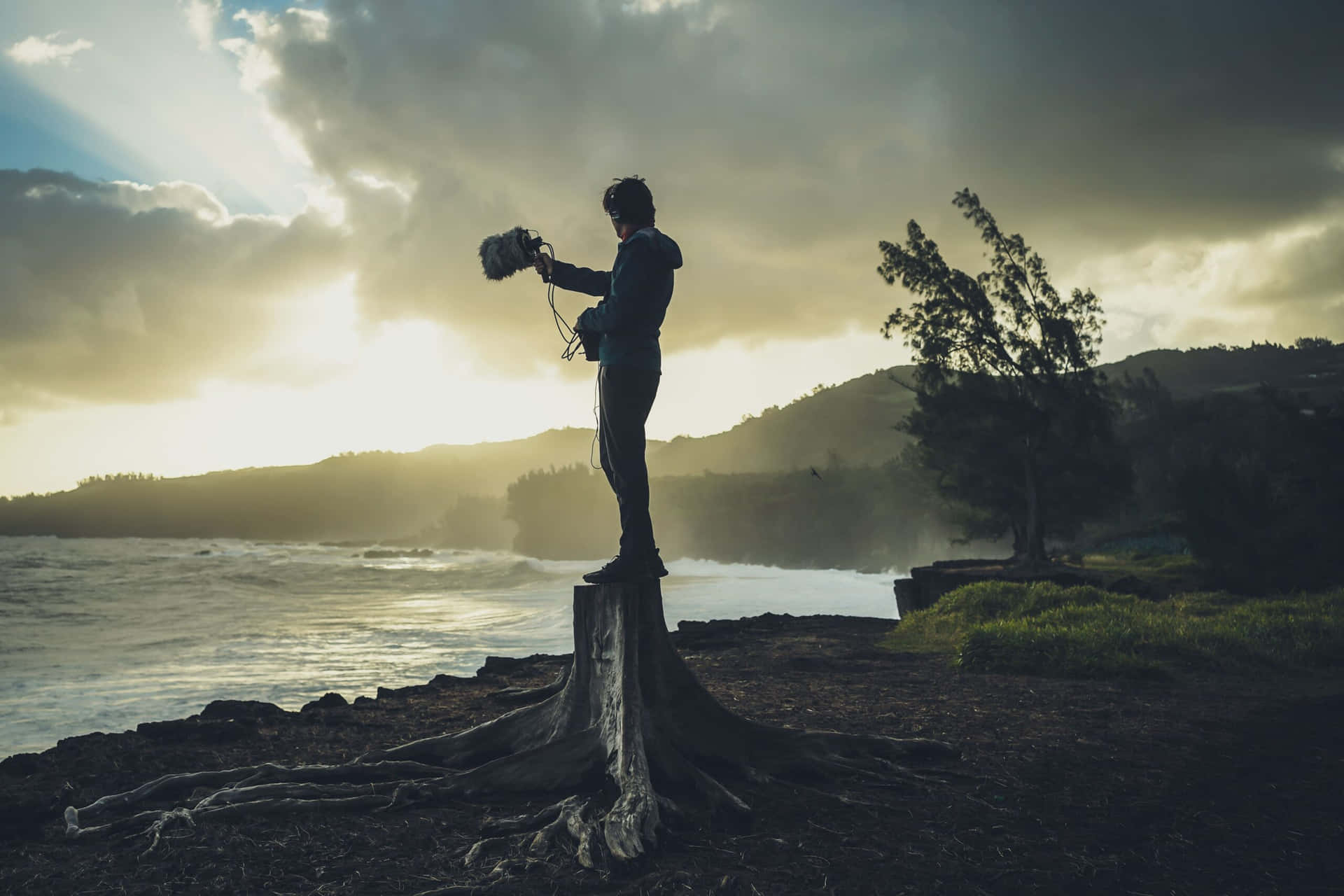 A Man Standing On A Tree Stump In Front Of The Ocean Wallpaper