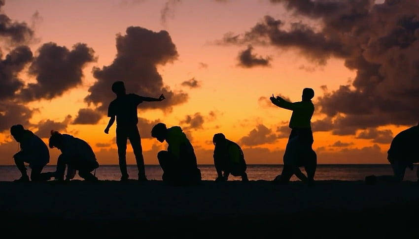 Silhuetter af mennesker på stranden ved solnedgang Wallpaper