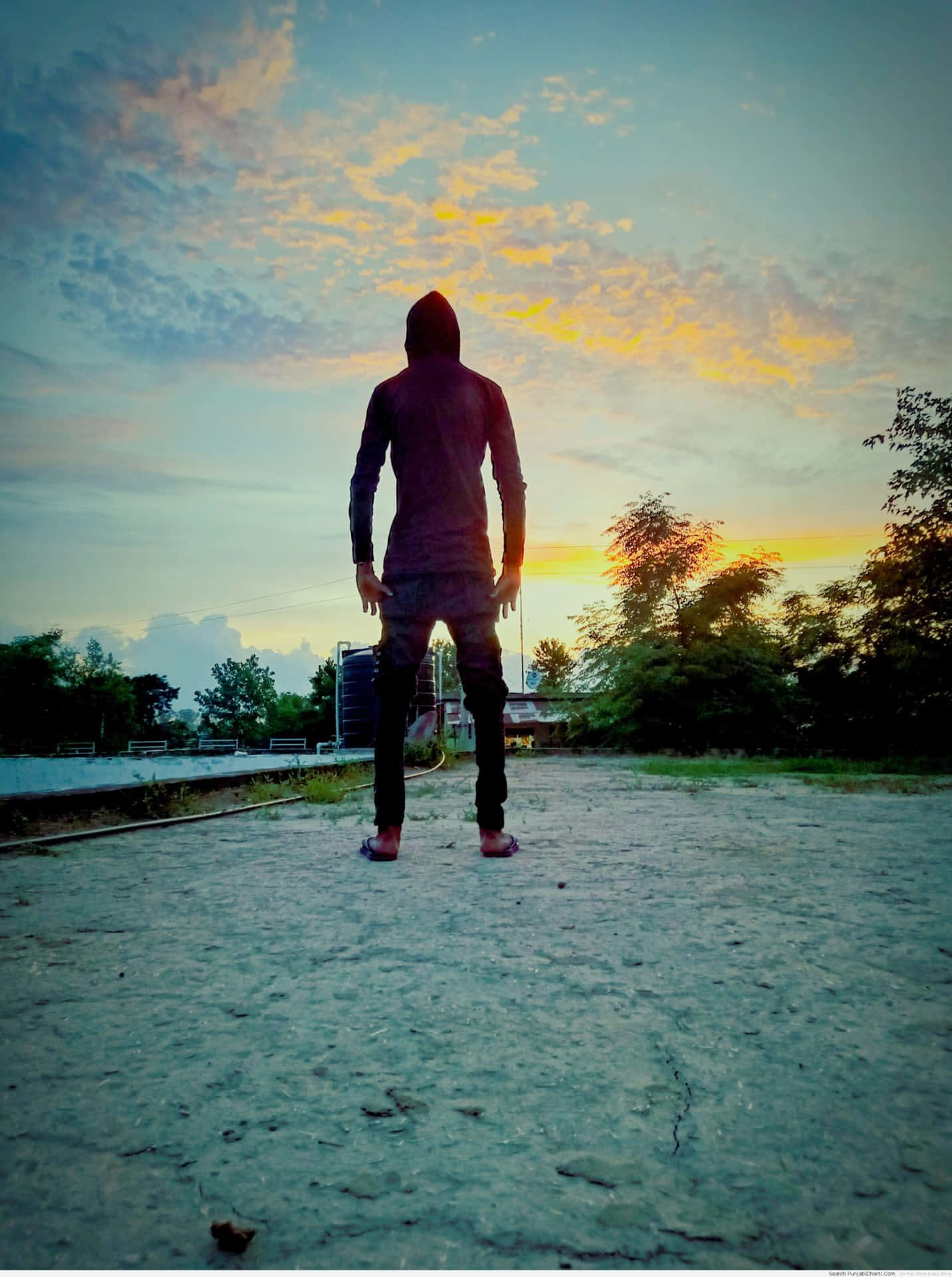 A Man Standing On A Dirt Road At Sunset
