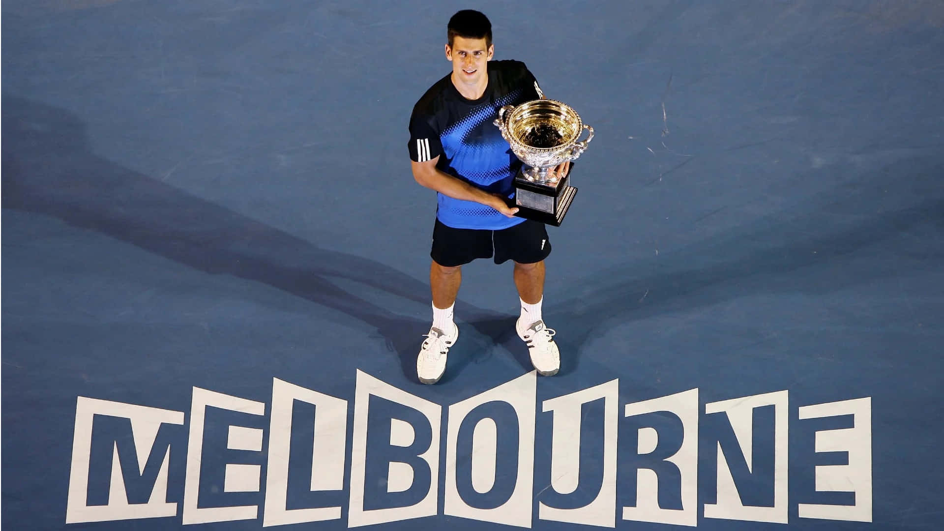A Tennis Player Holding A Trophy On A Blue Tennis Court