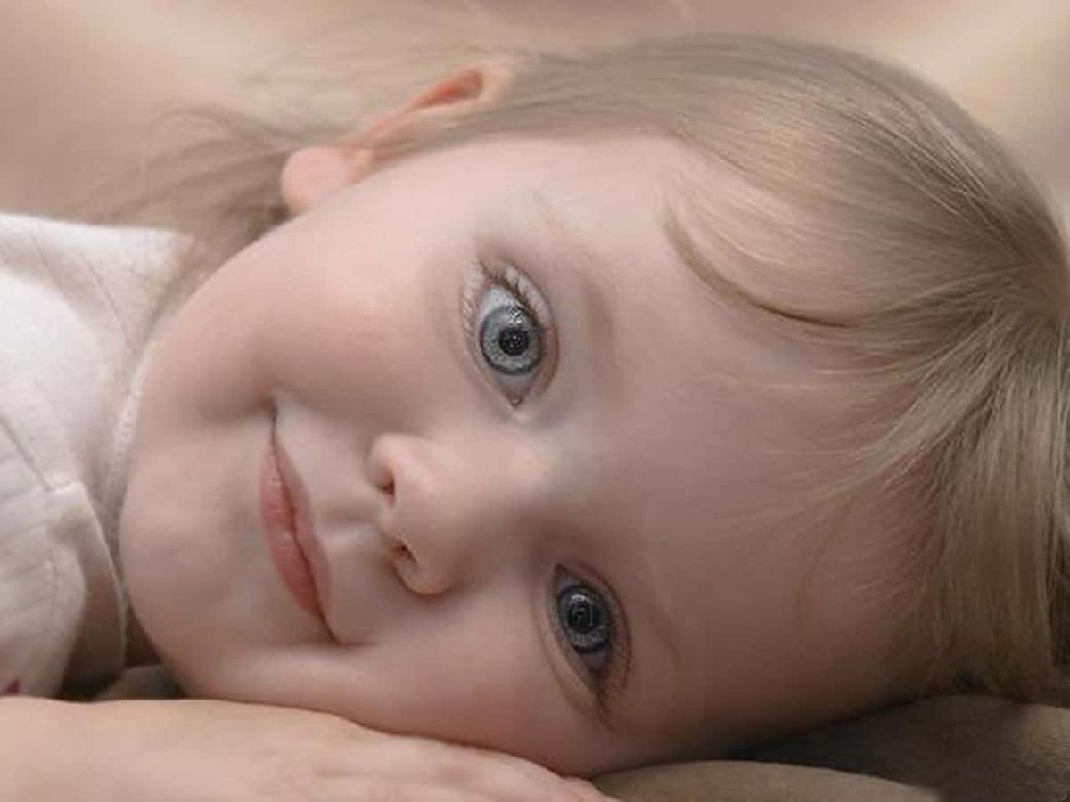 A Young Girl With Blue Eyes Laying On A Bed