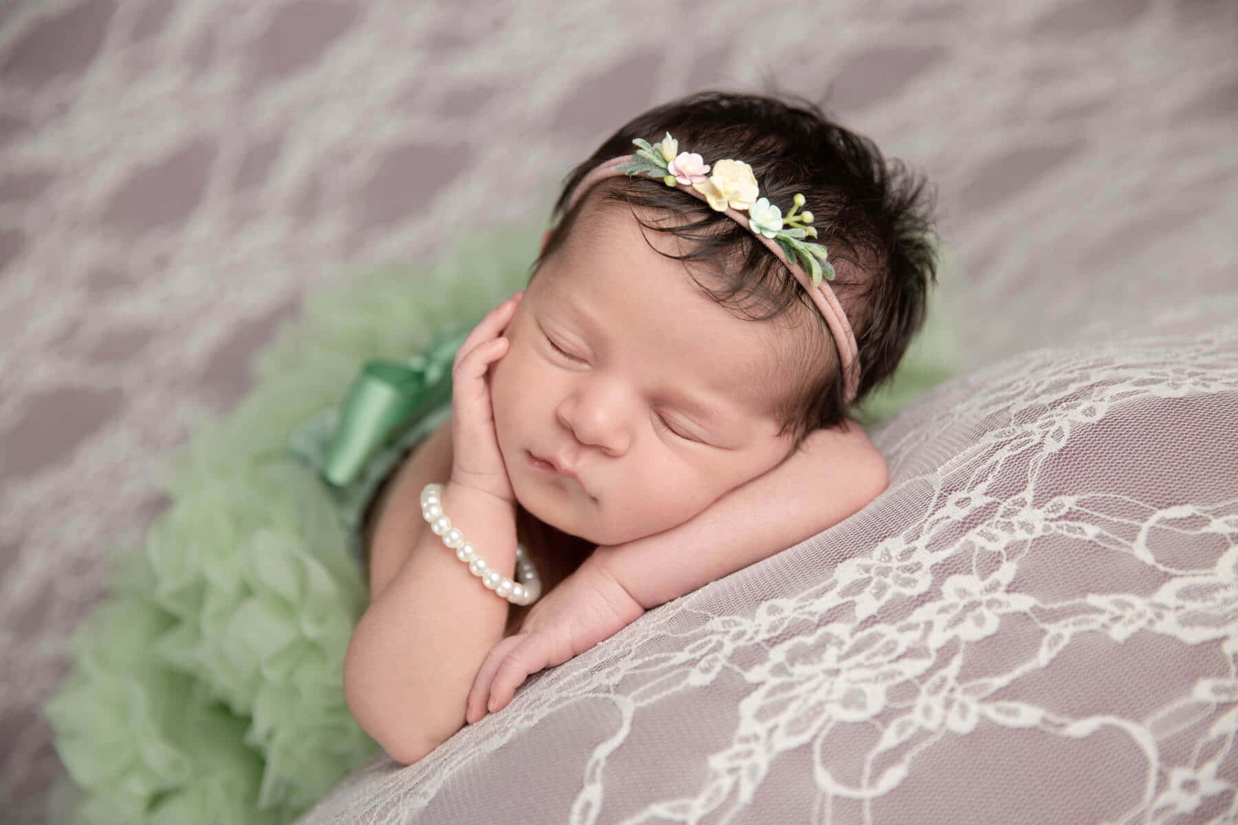 A Baby Girl In Green Tutu Laying On A White Blanket