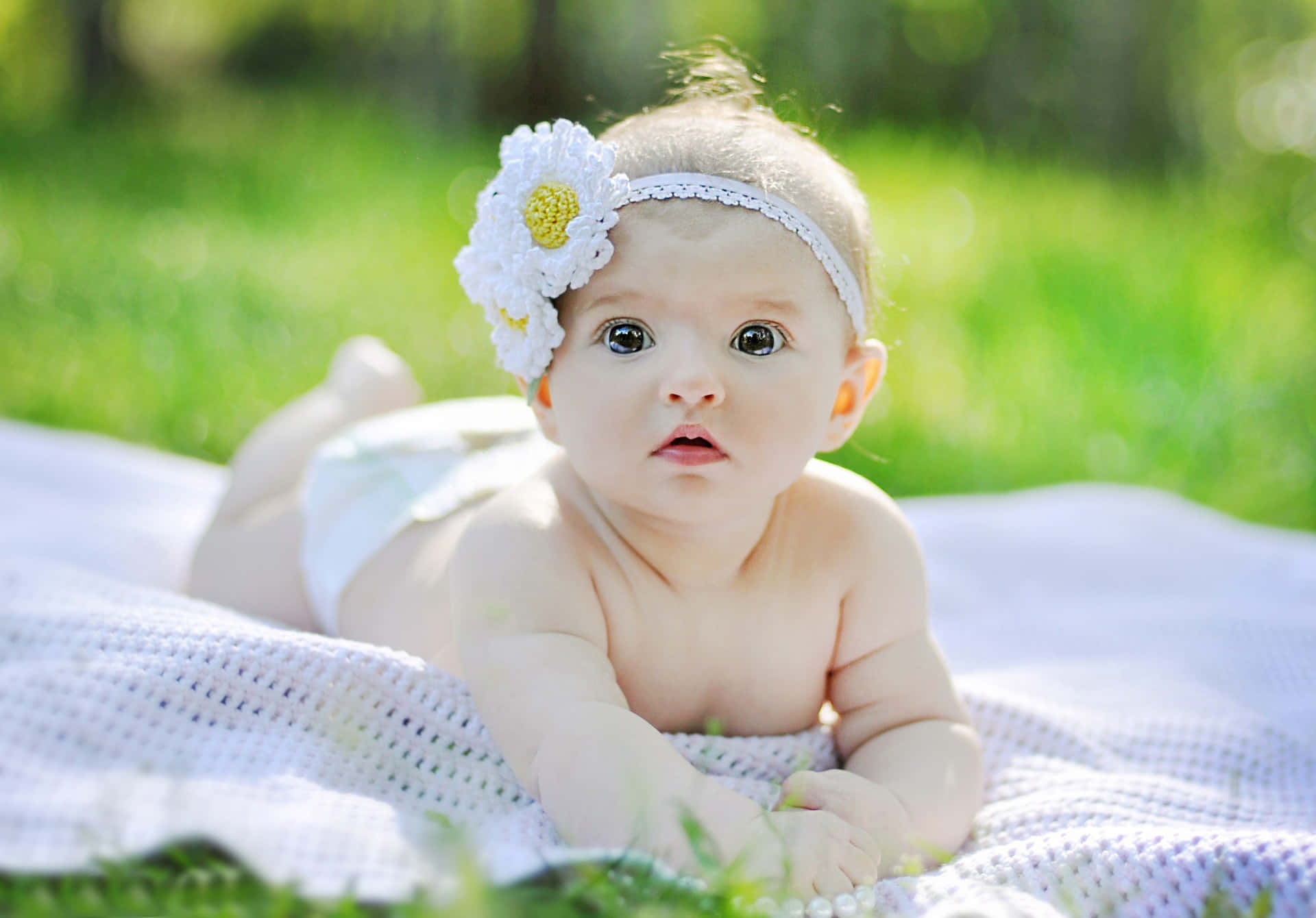 A Baby Girl Laying On The Grass With A Flower Headband