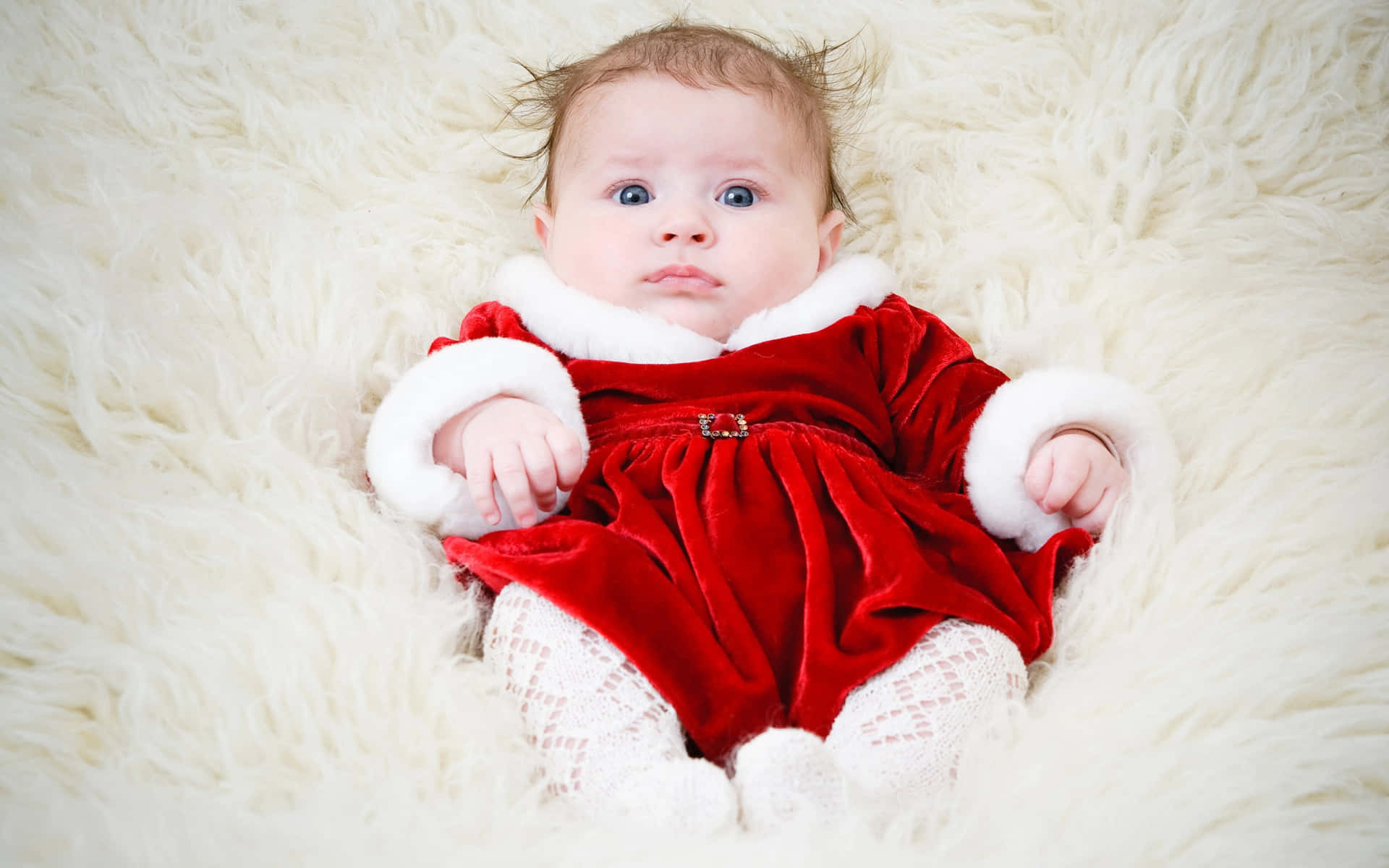 A Baby In A Red Santa Outfit Laying On A White Fur Rug