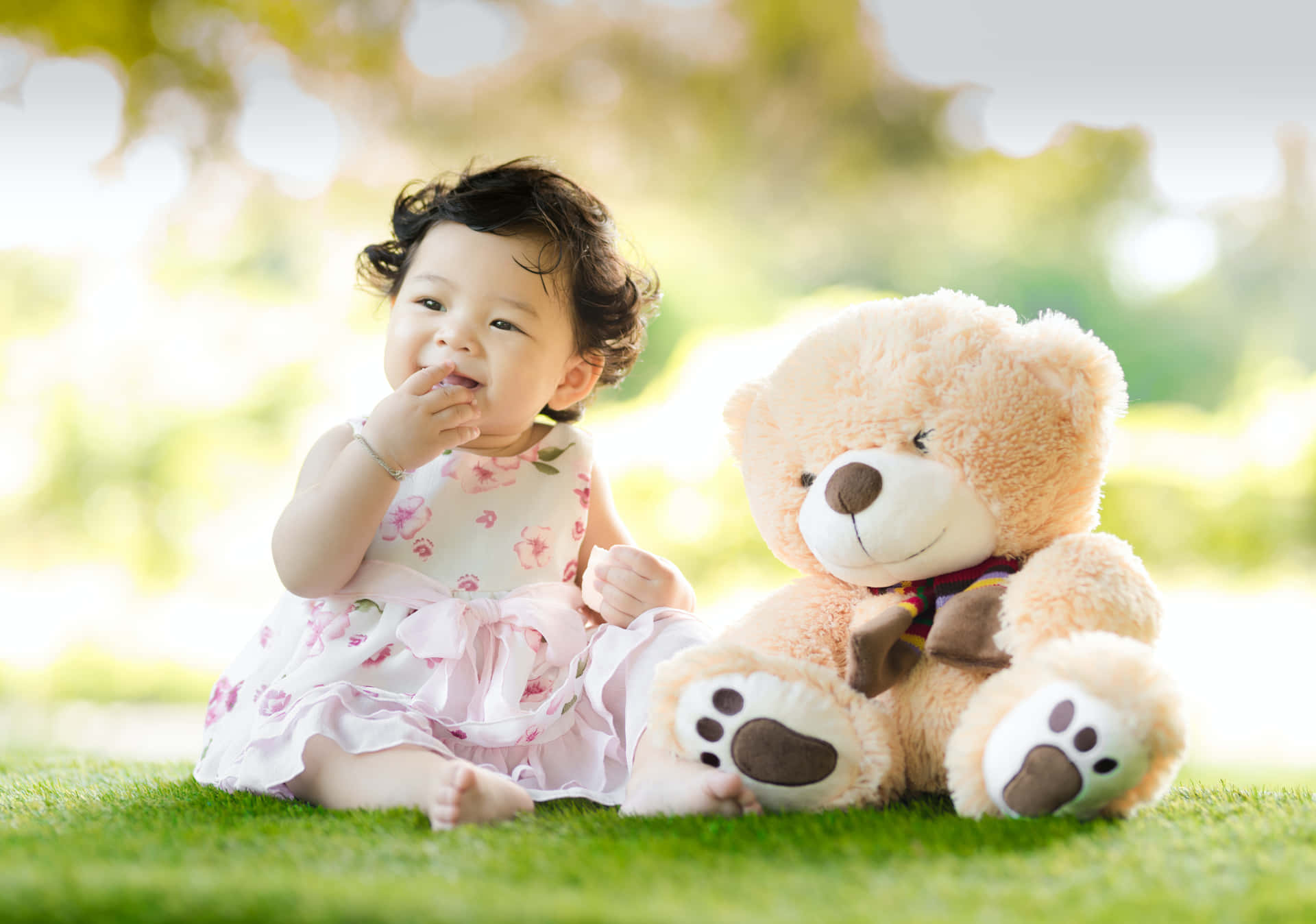 Adorable baby girl in white dress surrounded by soft toys and flowers