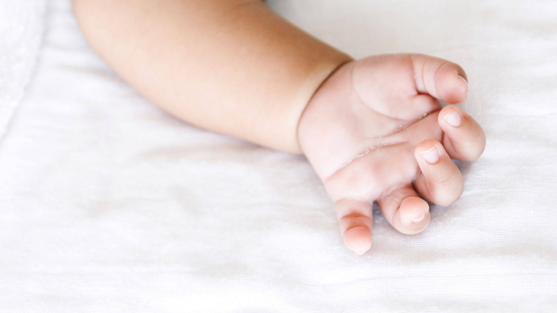 Baby Hand Resting On White Sheet Wallpaper