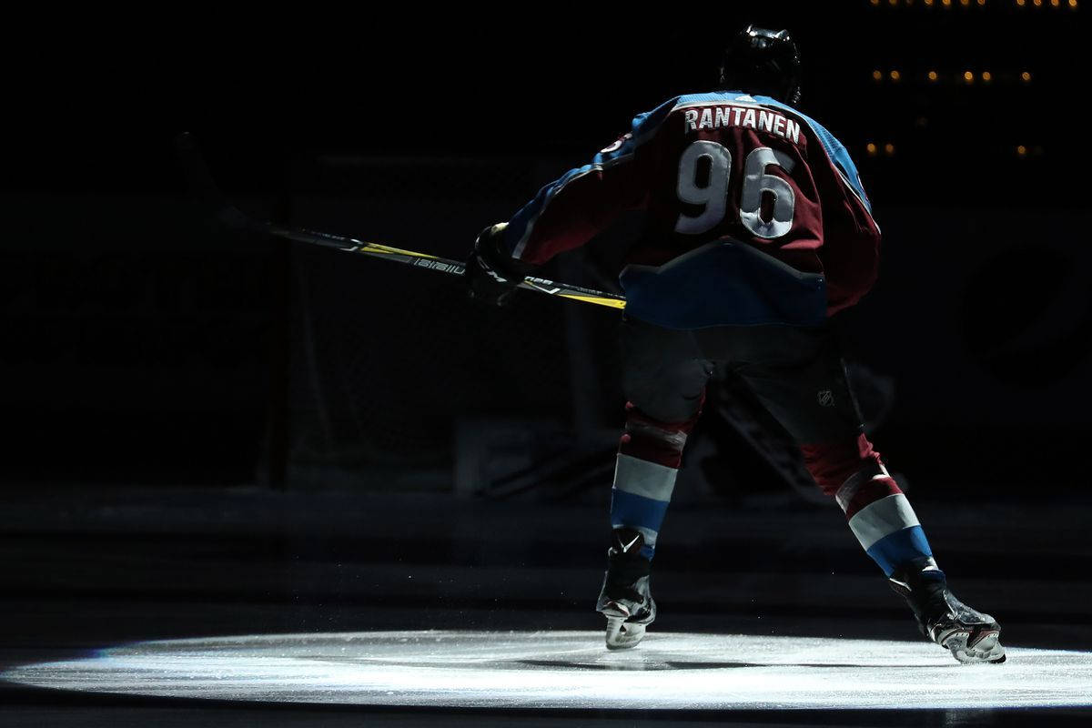 Back Shot Of Mikko Rantanen Raising Hockey Stick Under The Spotlight Wallpaper