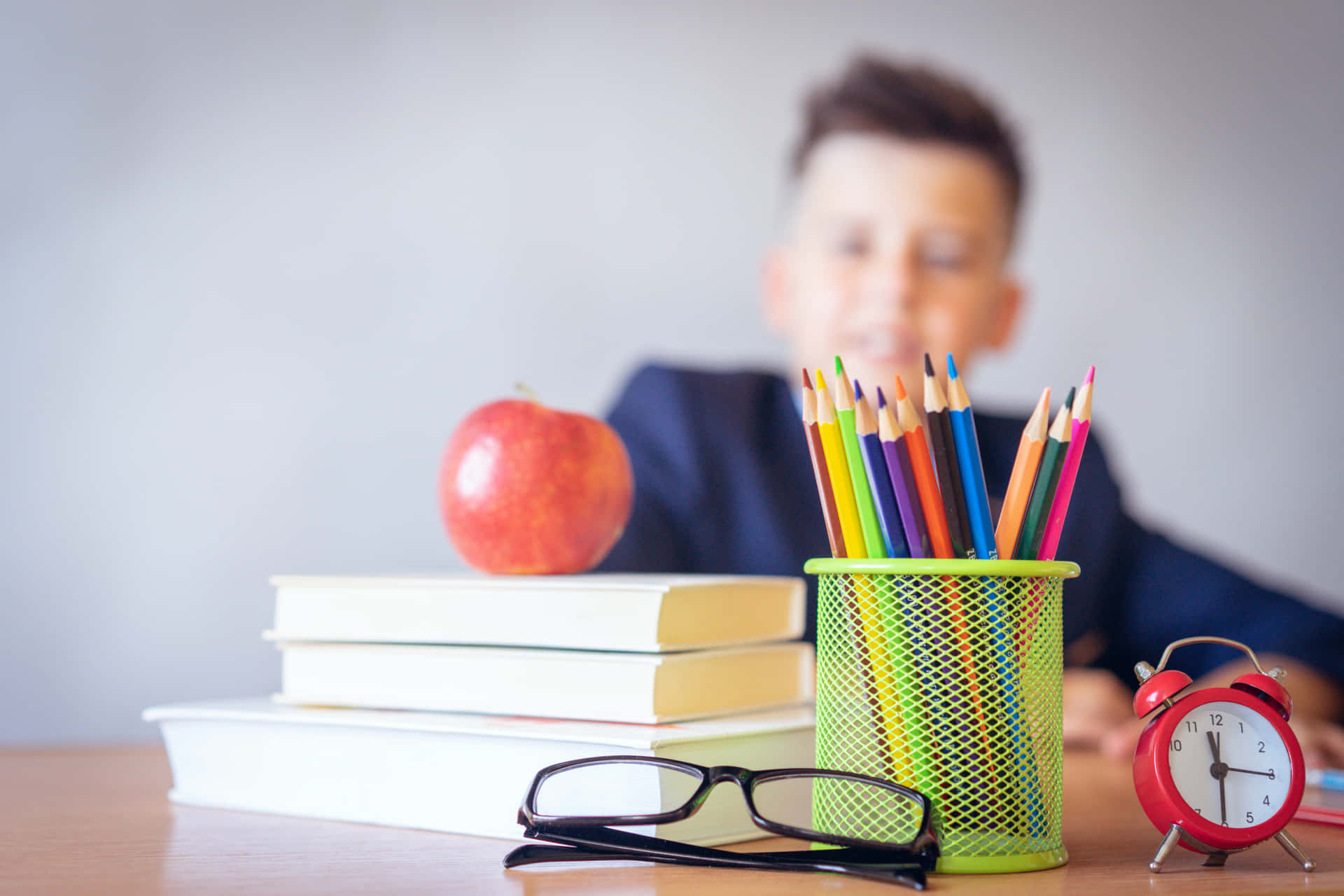 A Boy Is Sitting At A Desk With A Pencil, A Book And An Apple Wallpaper