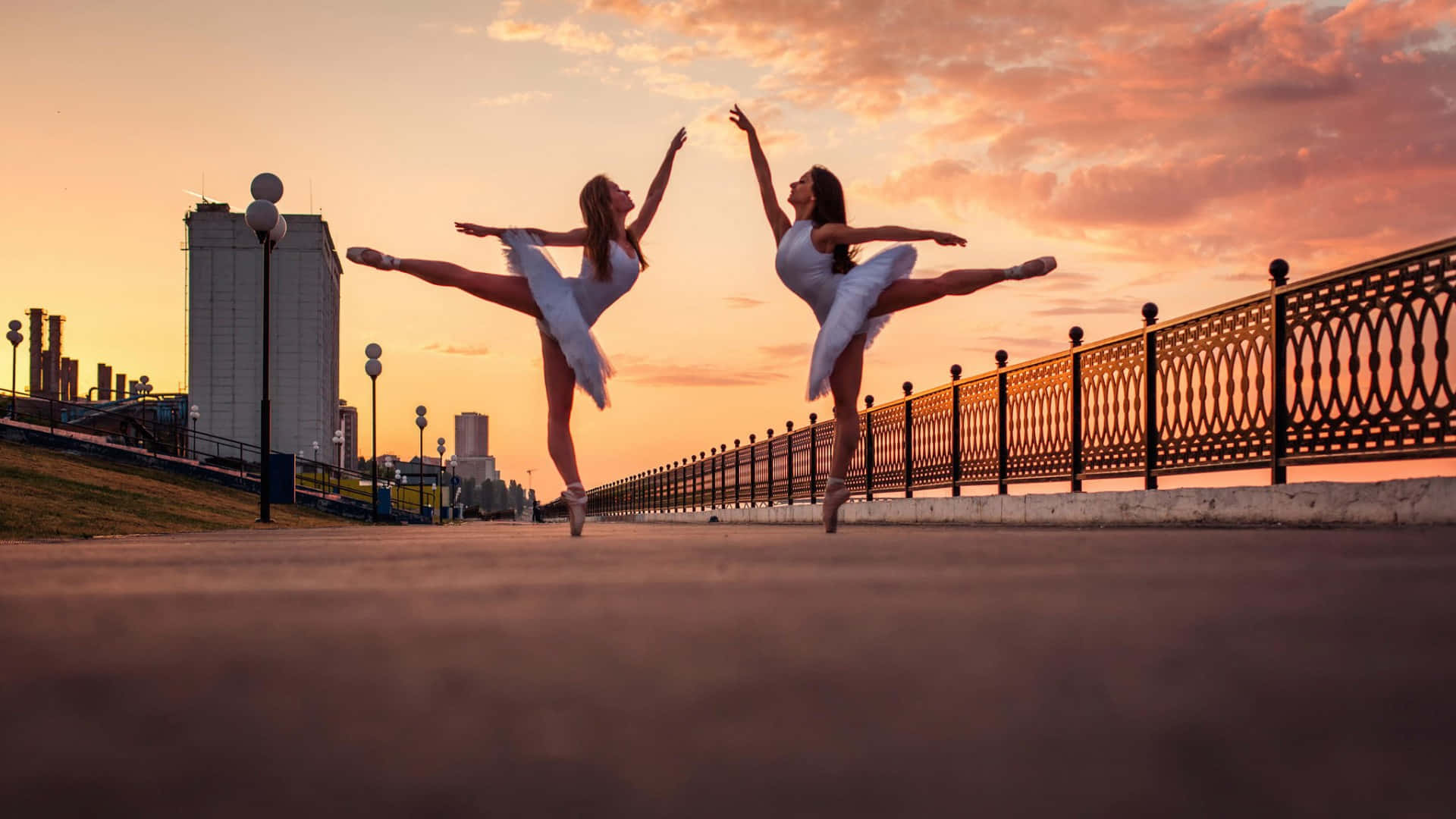 Two Ballerinas Are Dancing On The Street At Sunset
