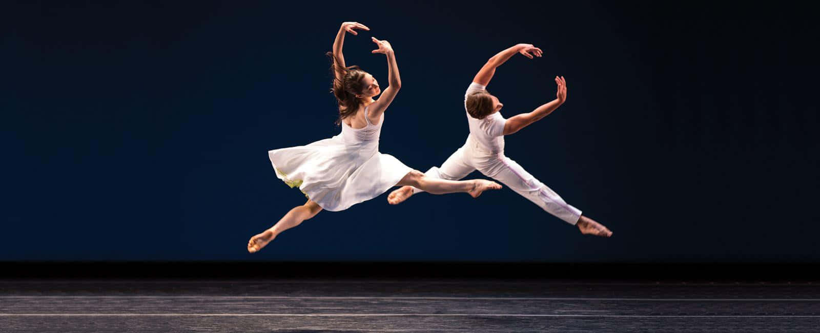Two Dancers In White Jump In The Air