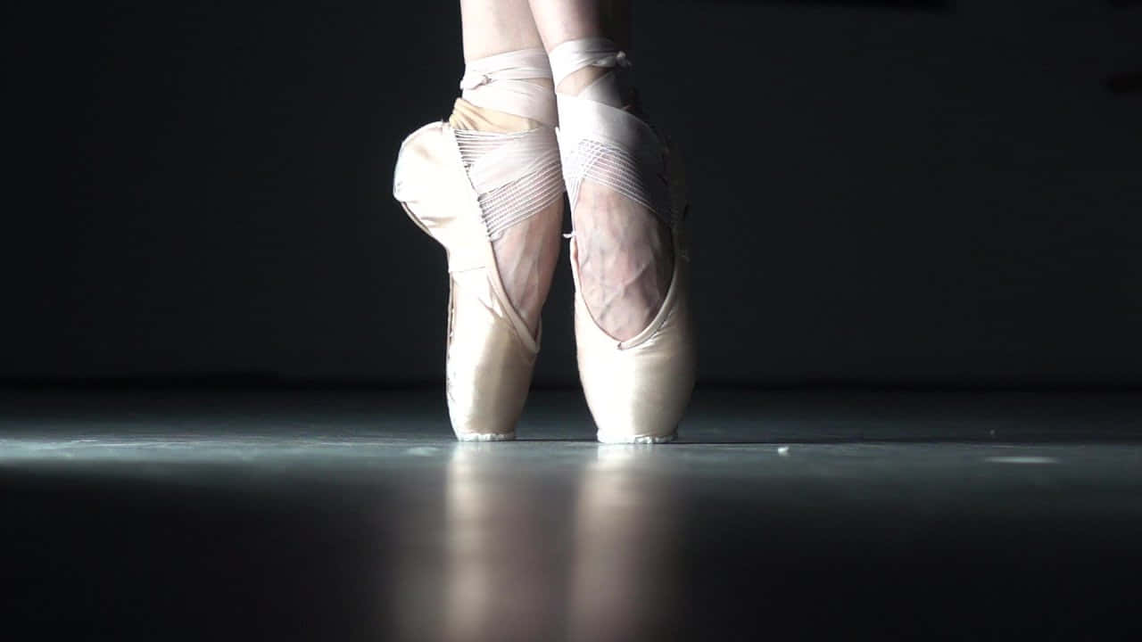 Lospies De Una Bailarina De Ballet Están Apoyados En Una Habitación Oscura. Fondo de pantalla