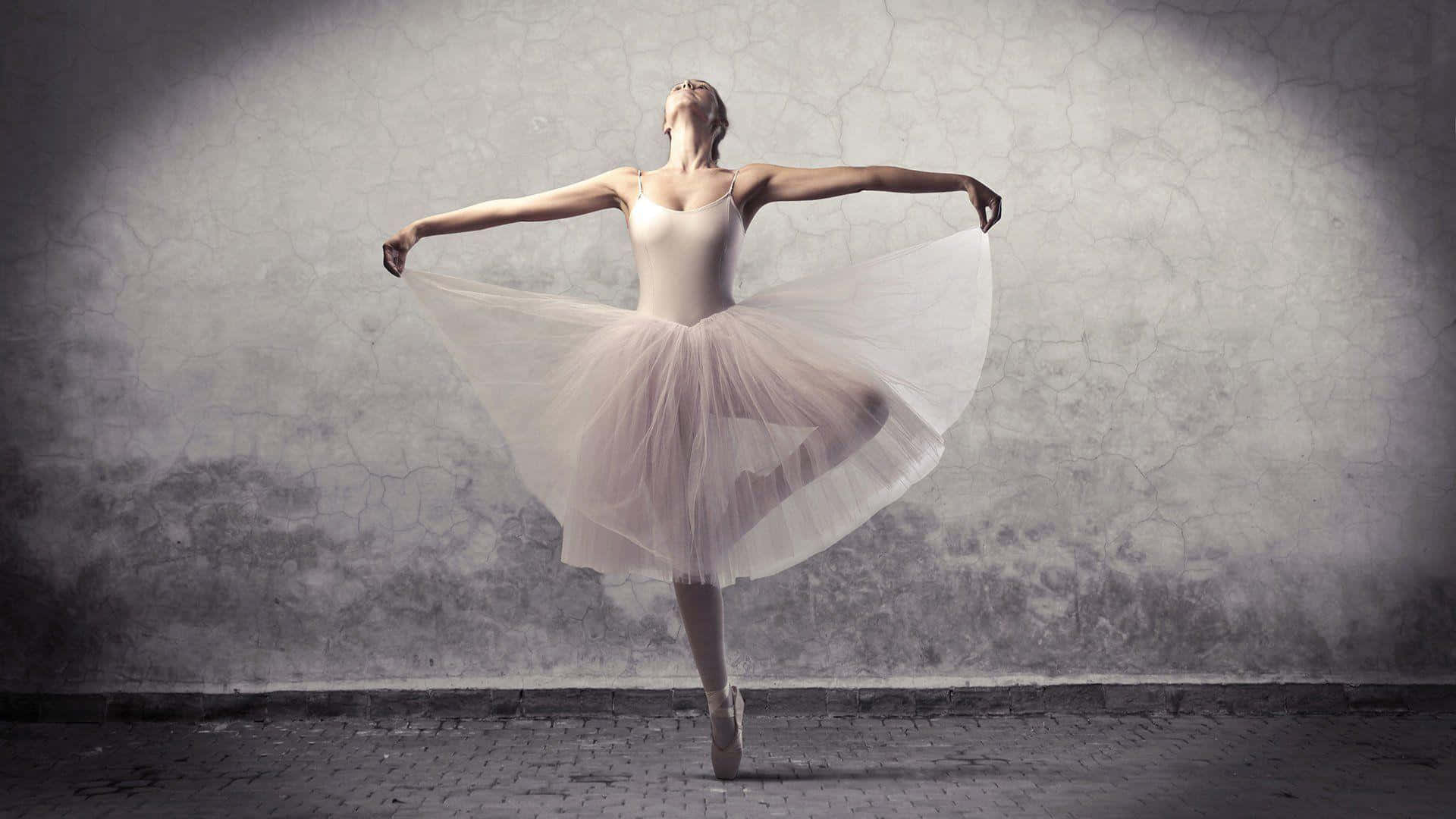 A graceful ballerina in her pink pointe shoes, on her toes in the dreamy swirl of a pirouette Wallpaper