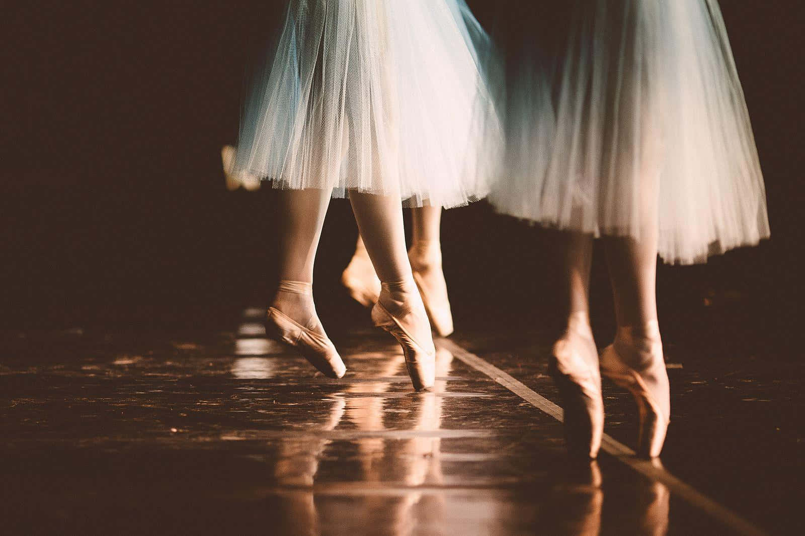 Bailarinesde Ballet En Tutús Caminando Sobre Un Piso Oscuro Fondo de pantalla
