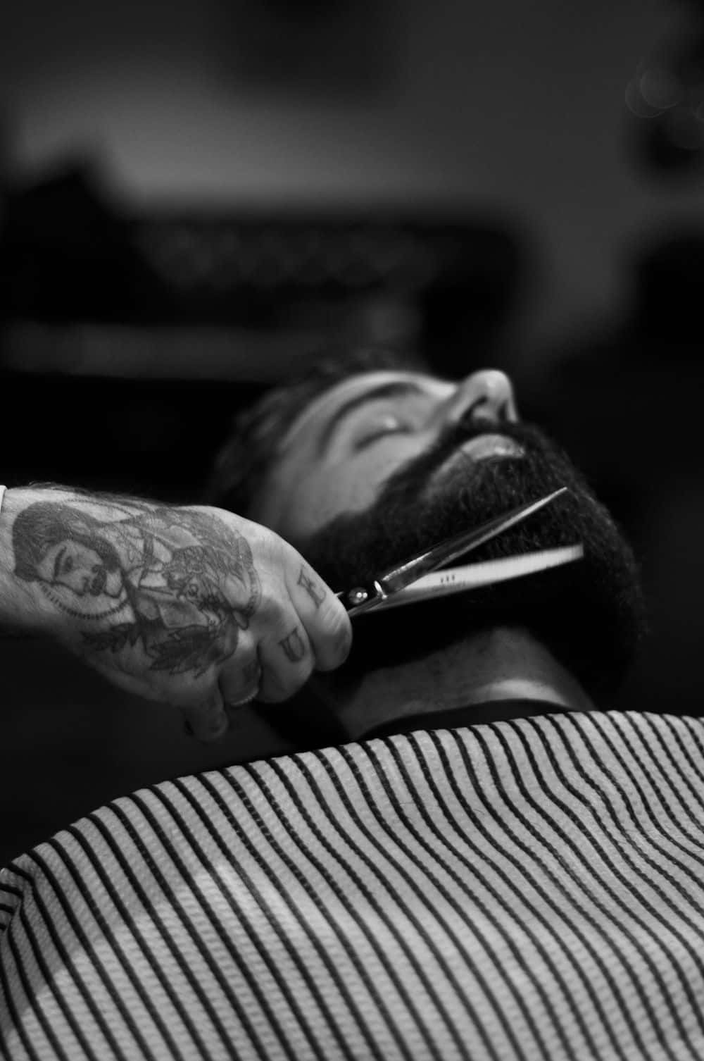 A Man Is Getting His Beard Cut By A Barber