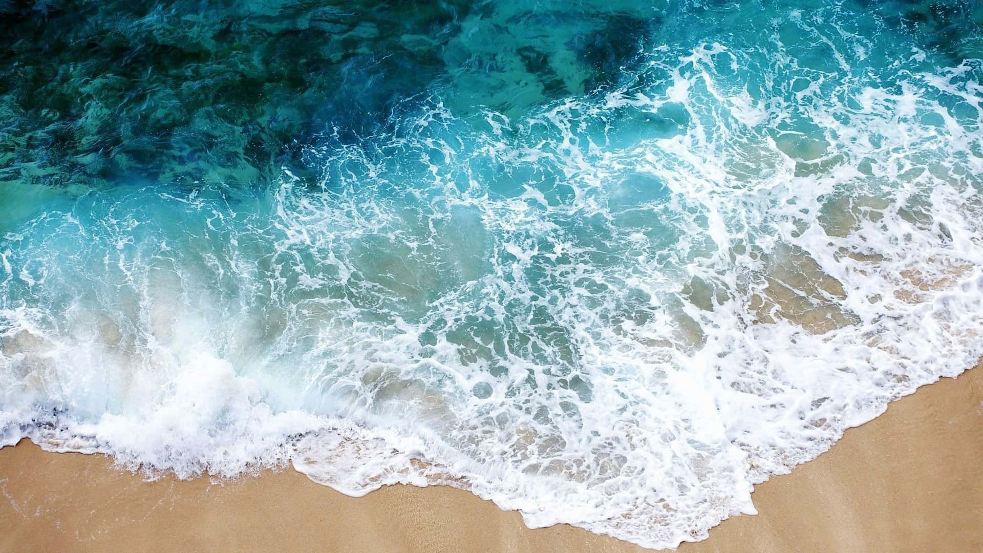 Et luftfoto af havbølger på en strand Wallpaper