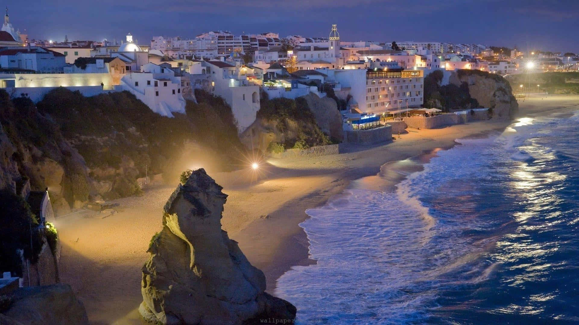 A City At Night With A Cliff And Ocean
