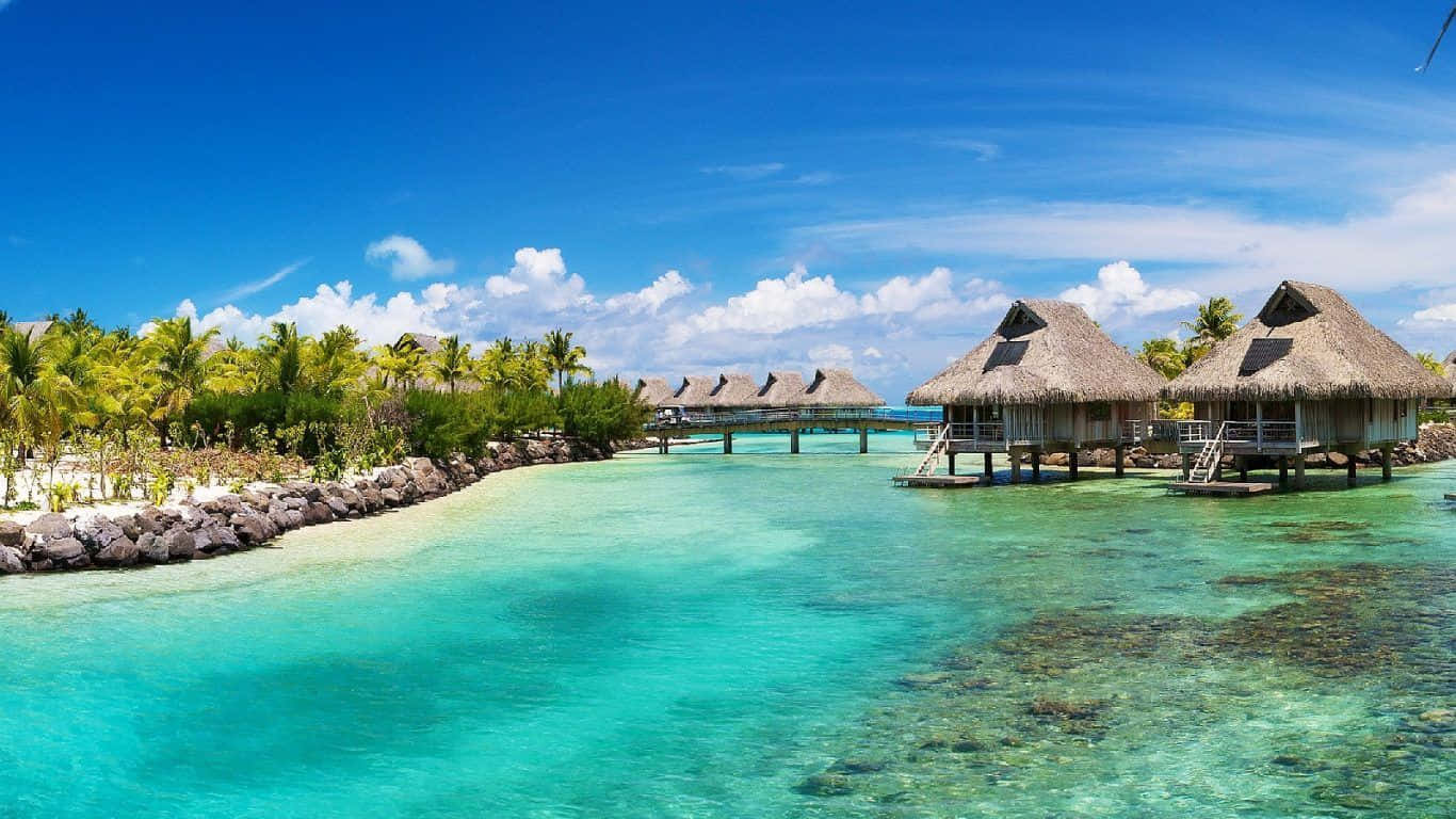 A Tropical Island With Thatched Huts And Clear Water Wallpaper