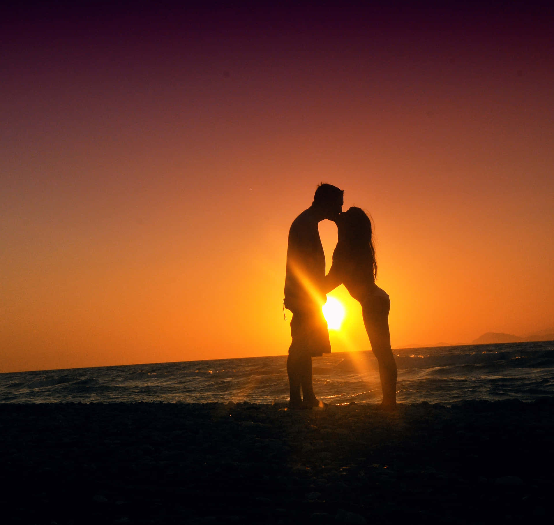 A couple enjoying a romantic walk on the beach at sunset Wallpaper