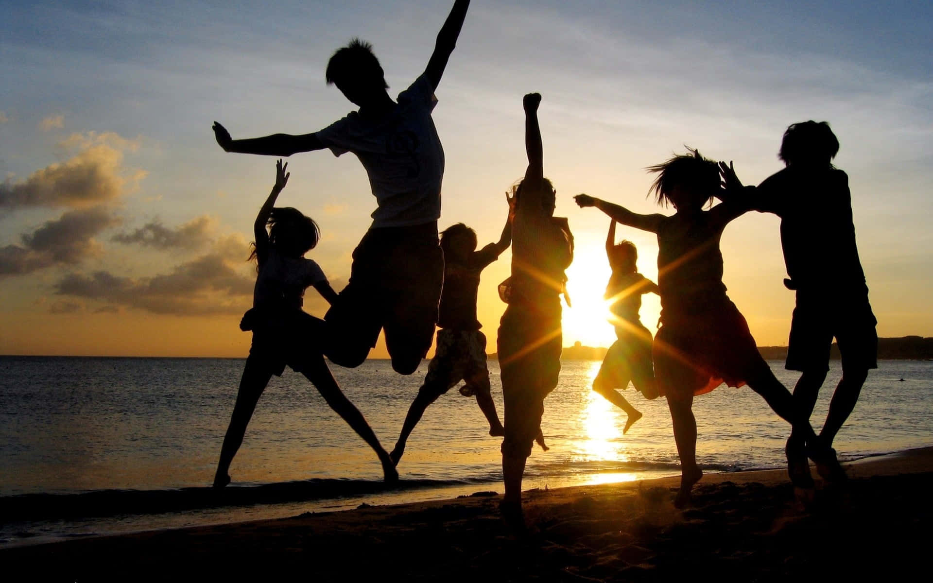 Friends having a fun and unforgettable beach party during sunset Wallpaper