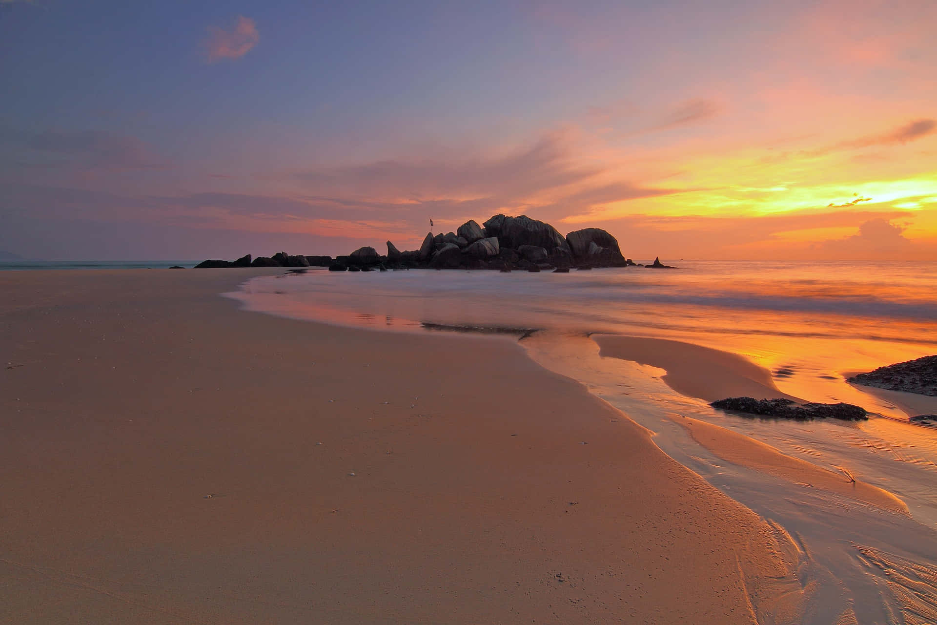 En strand med klipper og en solnedgang.