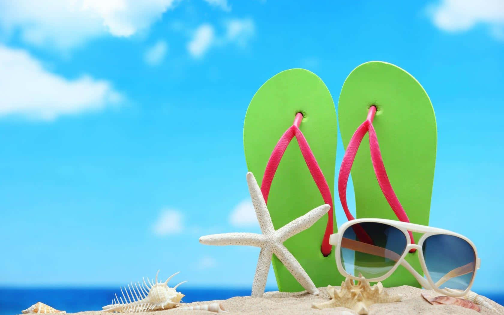 Pair of bright beach sandals on sandy shore Wallpaper