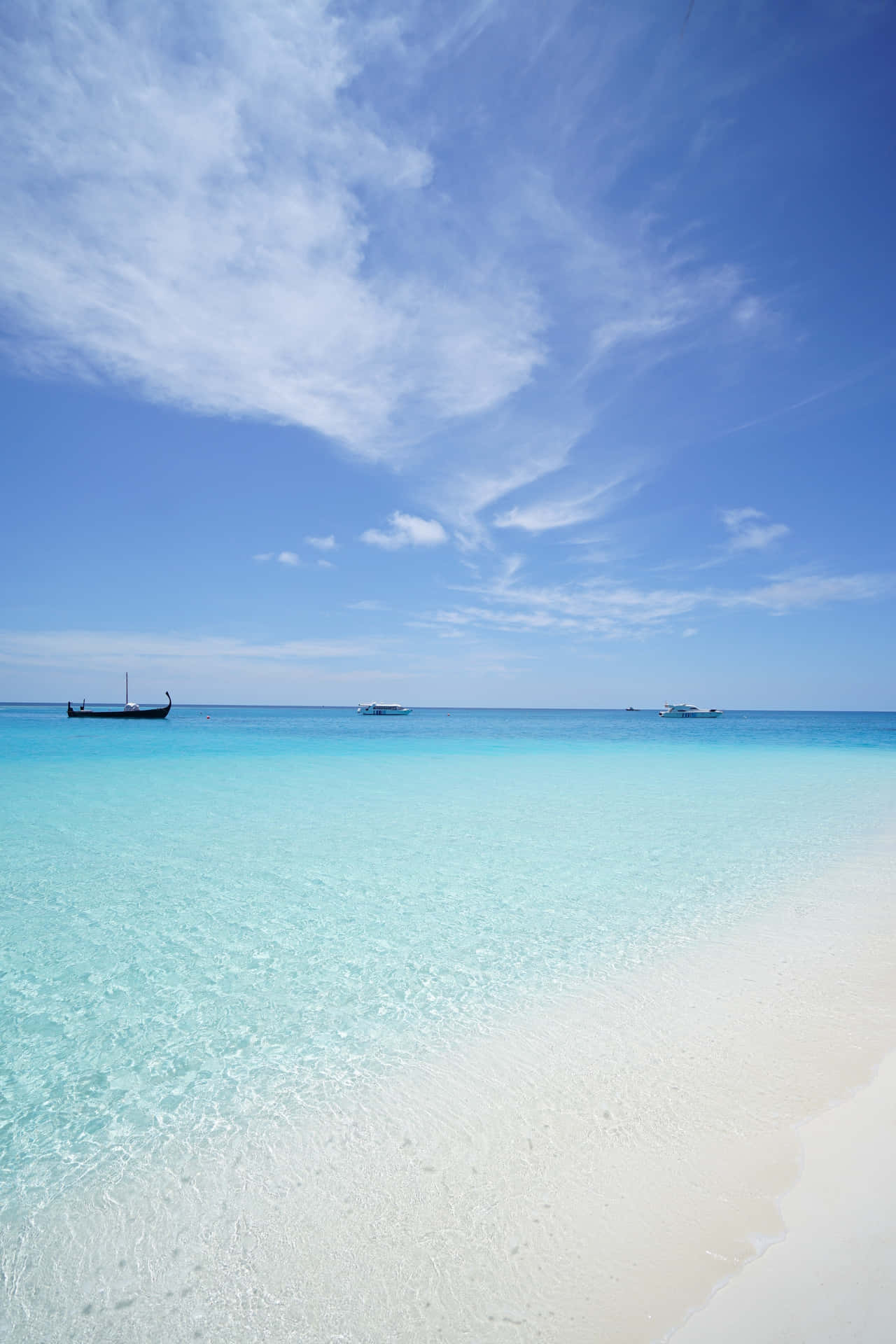 A Beach With Clear Water And A Boat In The Distance Wallpaper