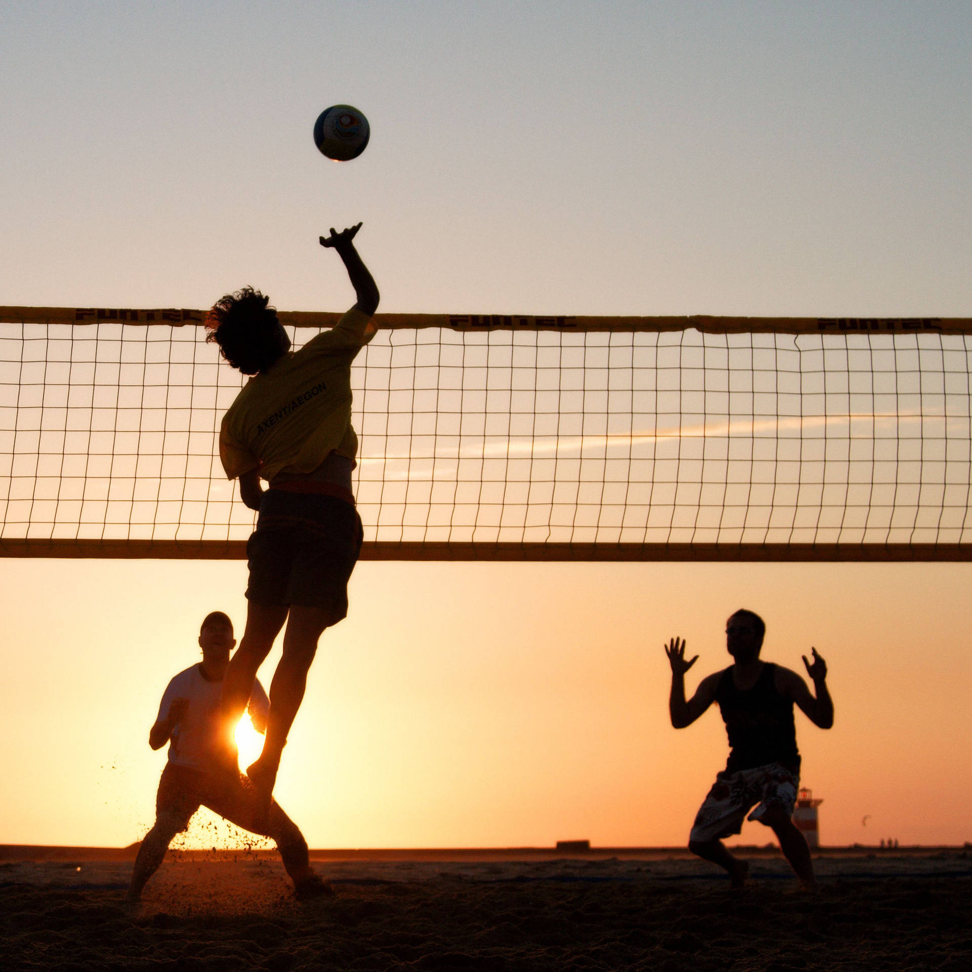 Silhouettedi Uomini Al Beach Volleyball Al Tramonto. Sfondo