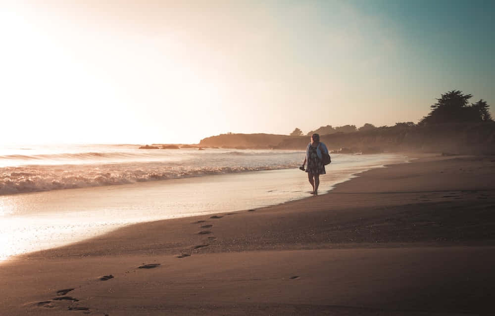 Een Serene Strandwandeling Tijdens Zonsondergang Achtergrond