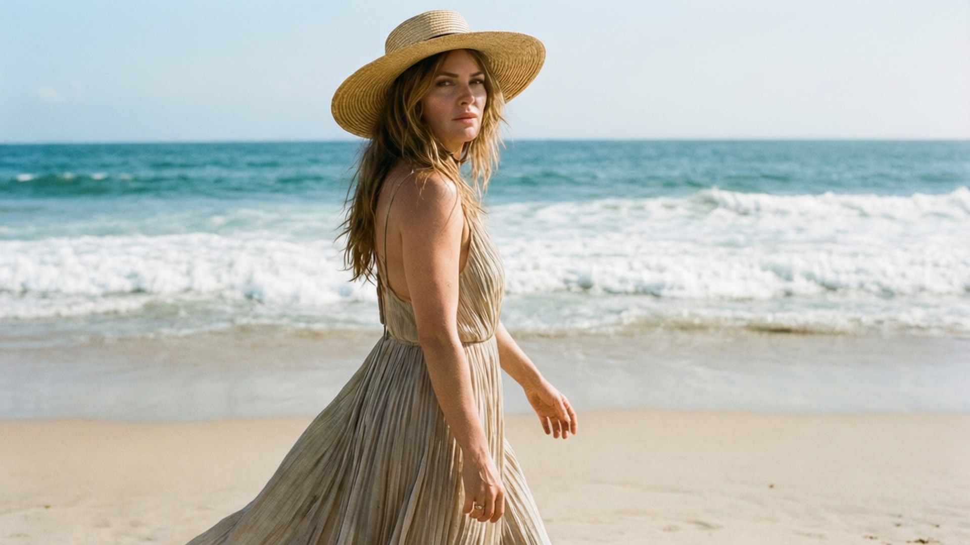 Strandspaziergang Hintergrundbilder — Mandy Moore geht an einem sonnigen Strand in einem fließenden Sommerkleid und Strohhut.