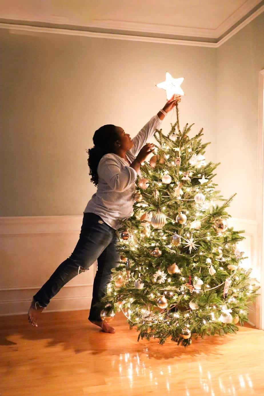 Einefrau Setzt Einen Stern Auf Einen Weihnachtsbaum.