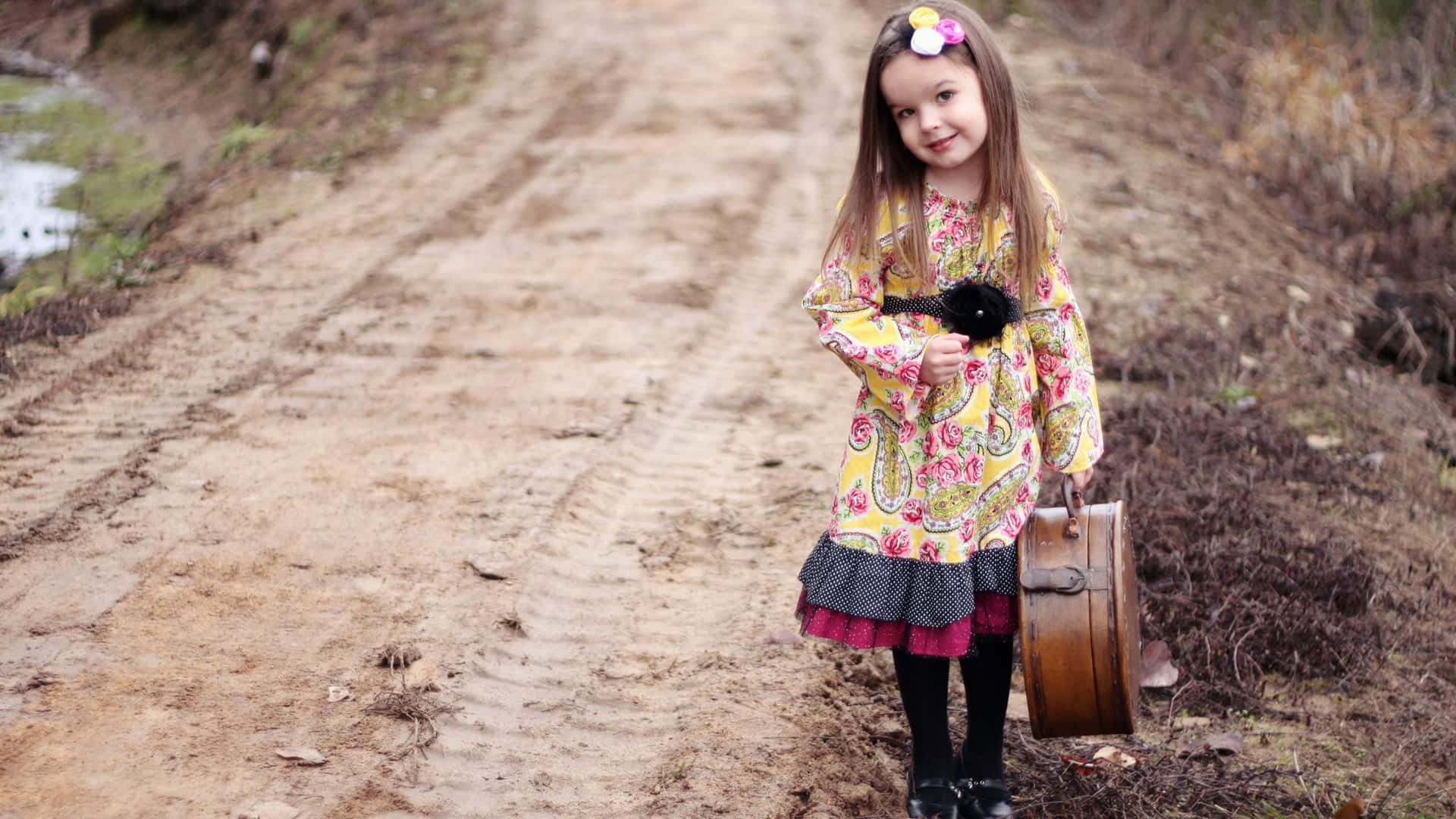 A Little Girl Holding A Suitcase On A Dirt Road