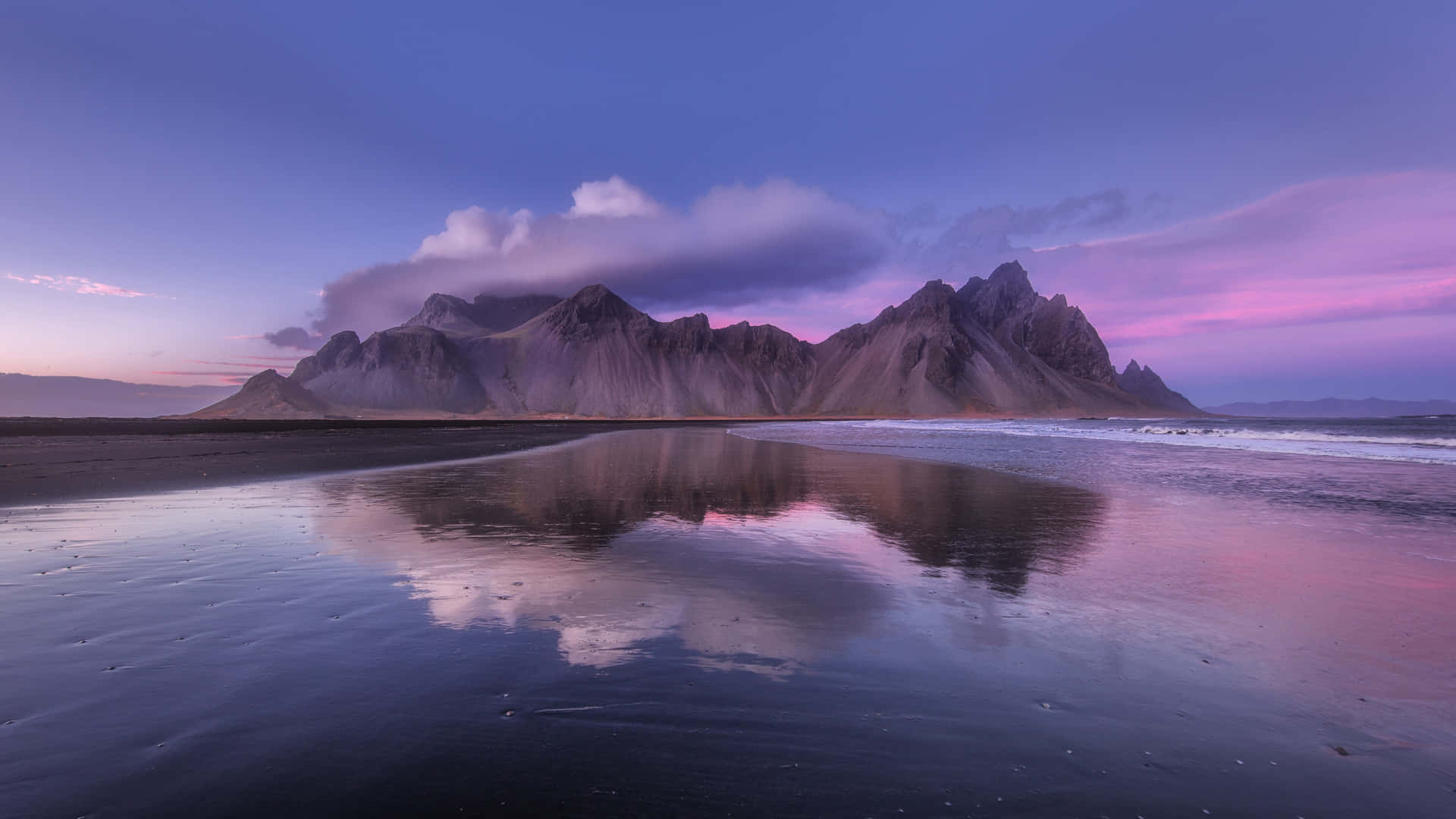 A Mountain Range Is Reflected In The Water At Sunset Wallpaper