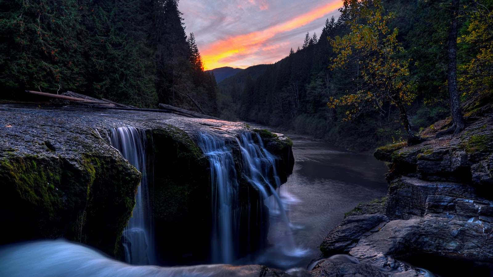 a waterfall in the forest at sunset