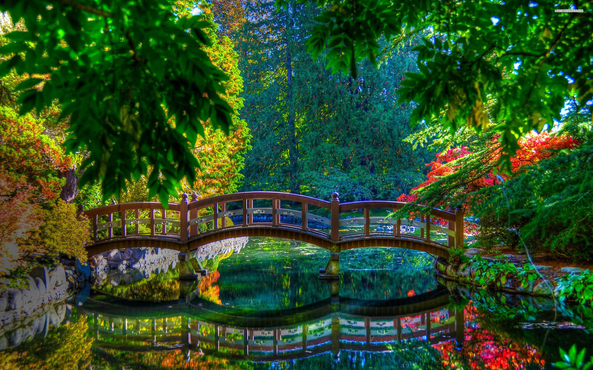 A Wooden Bridge Surrounded By Green Trees And Flowers