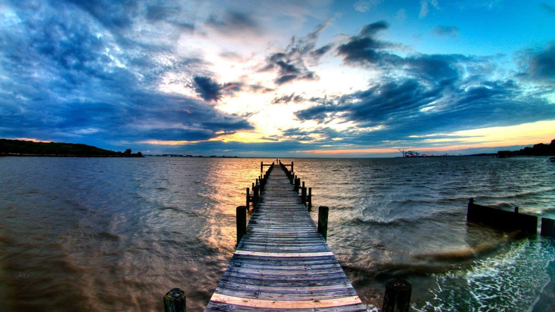 a dock leading into the water with clouds in the sky
