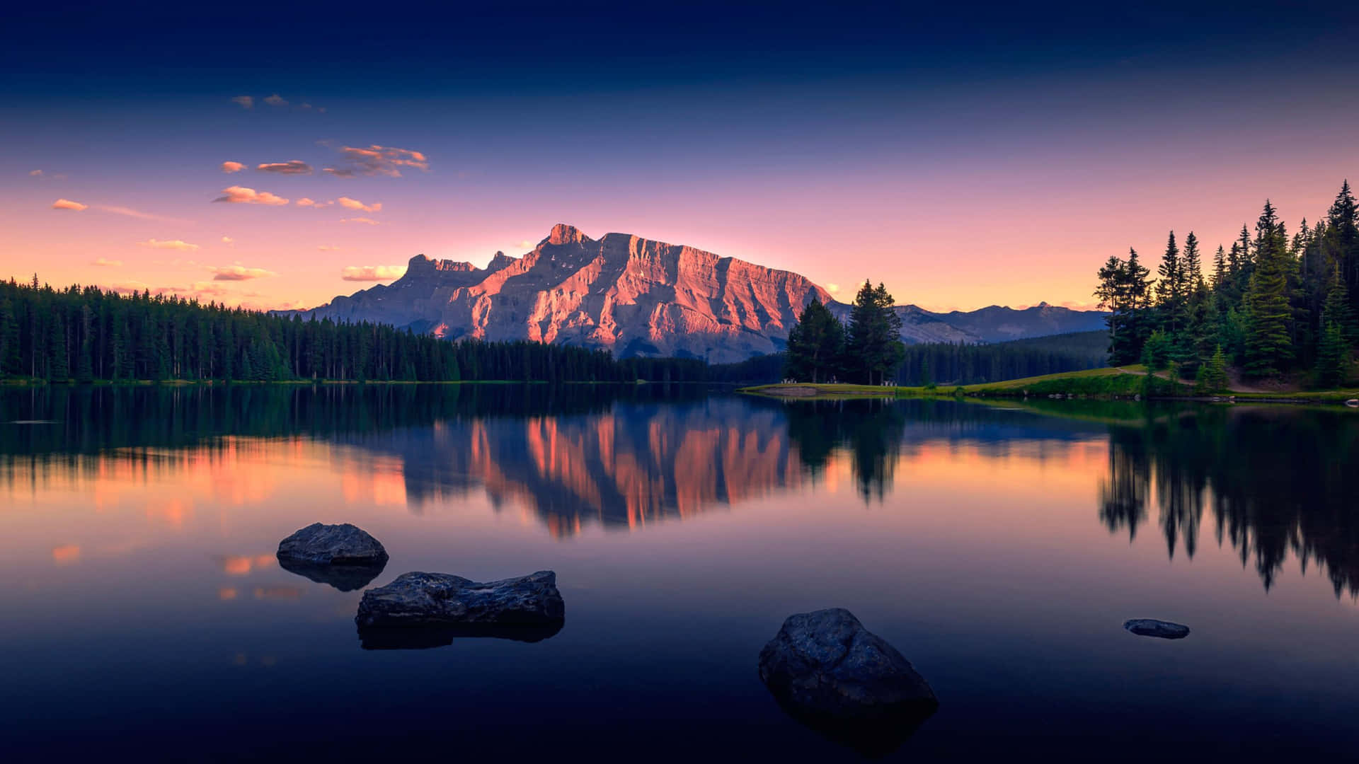 a mountain lake with rocks and trees at sunset
