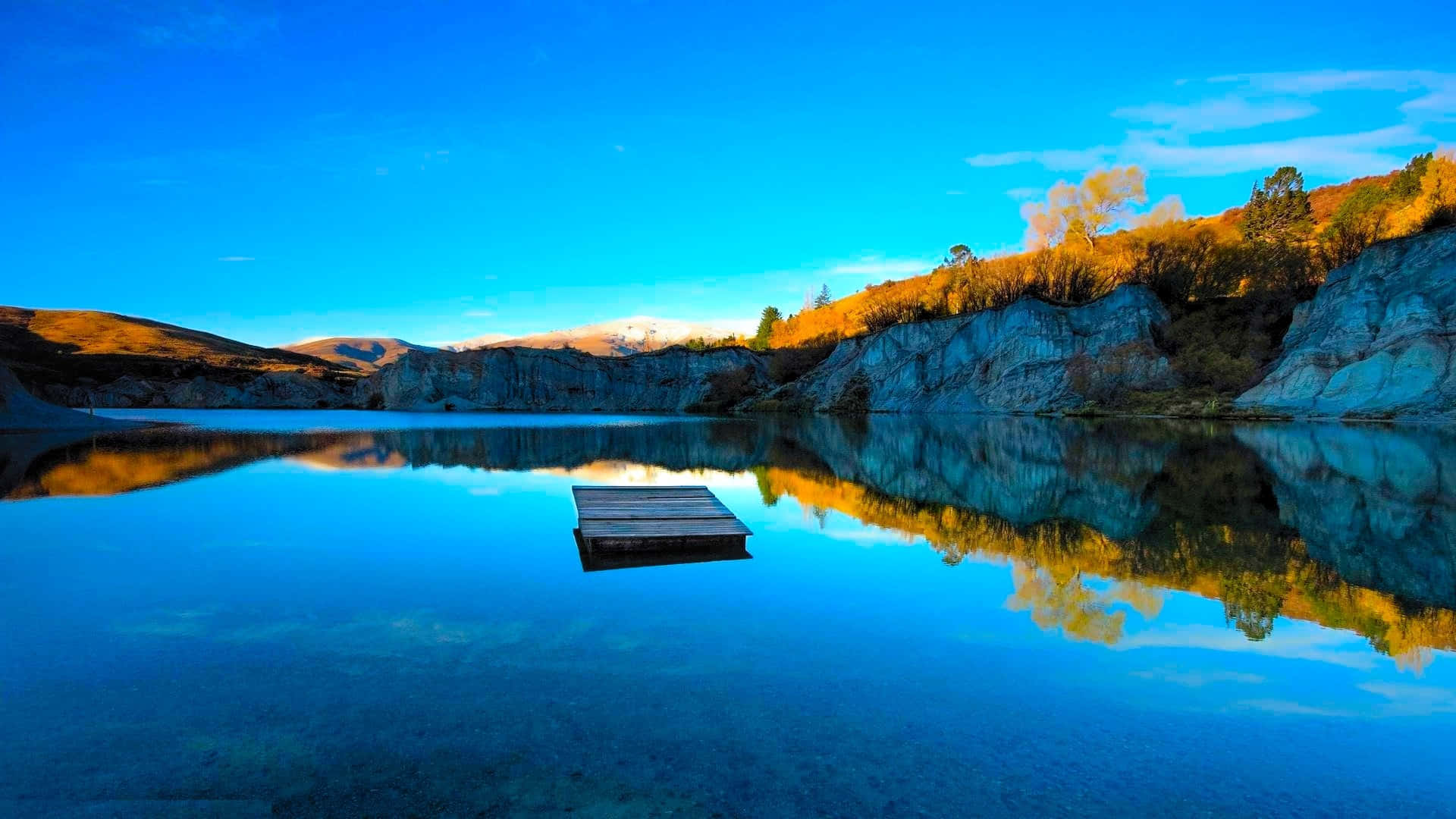 a dock is reflected in a lake with mountains in the background