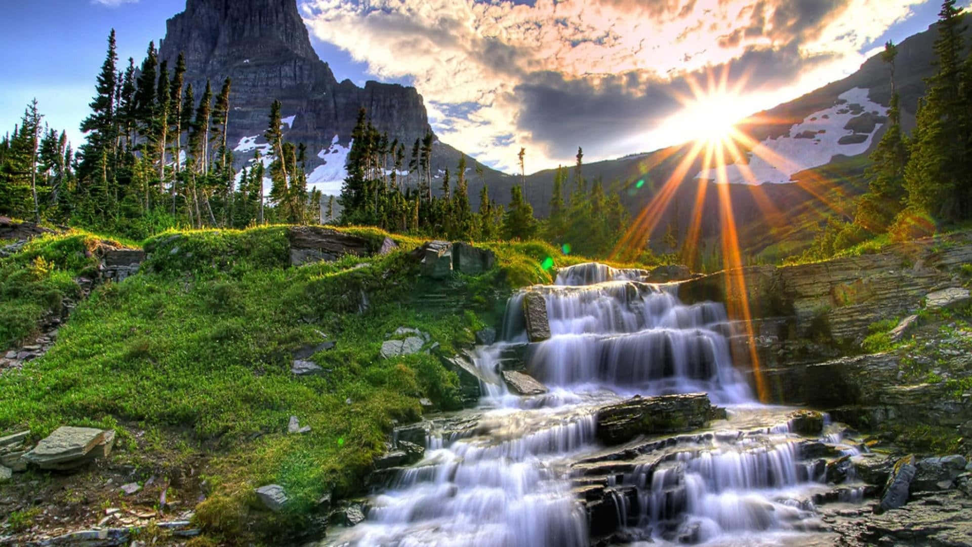 a waterfall in the mountains with the sun shining on it