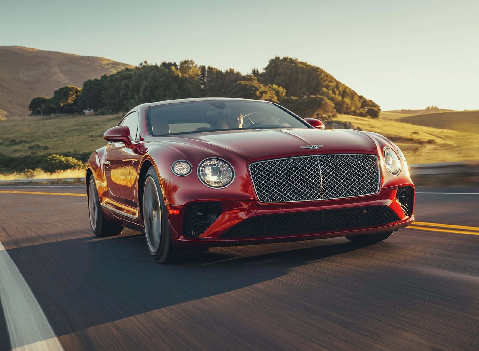 The Red Bentley Continental Gt Is Driving Down A Road