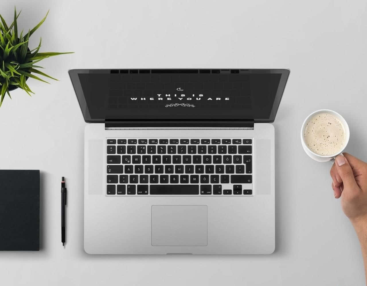 En laptop med en kop kaffe og et notatbog på et bord