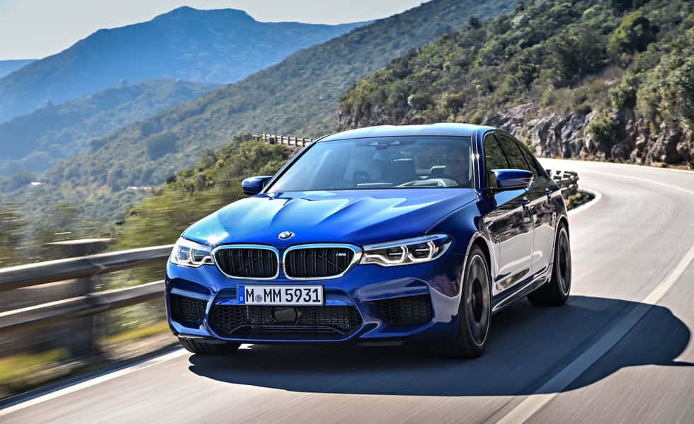 The Blue Bmw M5 Is Driving Down A Mountain Road