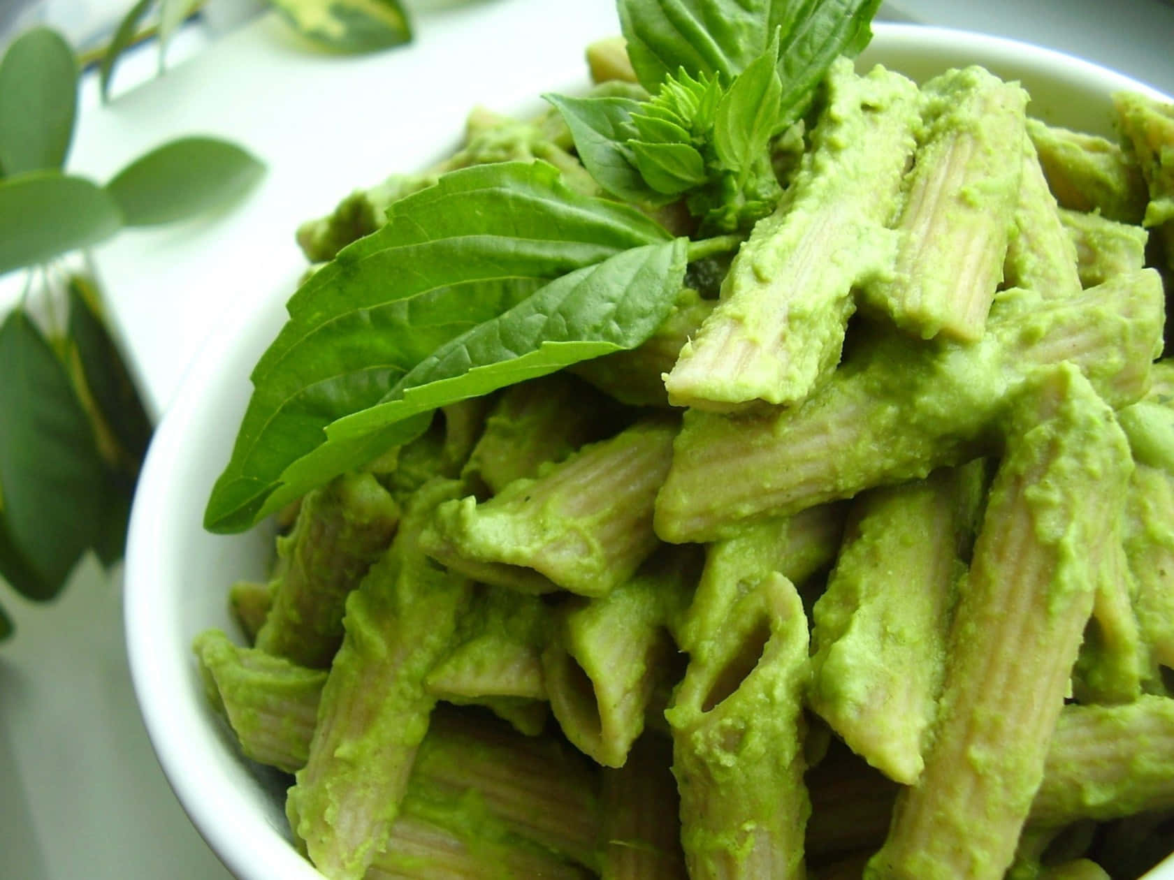 A Bowl Of Pasta With Pesto And Basil Leaves